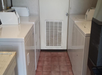 Laundry room with four white washing machines and dryers facing each other, a door with a vent in the center, and tiled flooring.