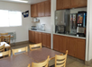 A dining area with wooden tables and chairs, cabinets, a toaster, an ice machine, and a beverage dispenser. A "Bear Country" sign is on the wall.