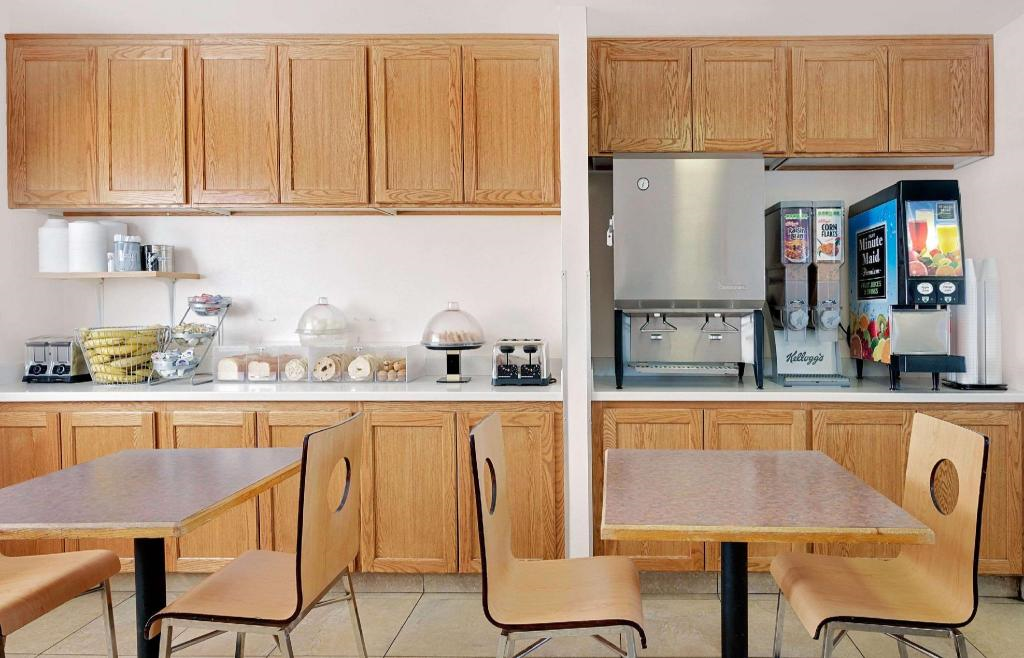 Breakfast area with wooden cabinets, tables, chairs, a cereal dispenser, baked goods display, juice machine, and coffee station on a countertop.