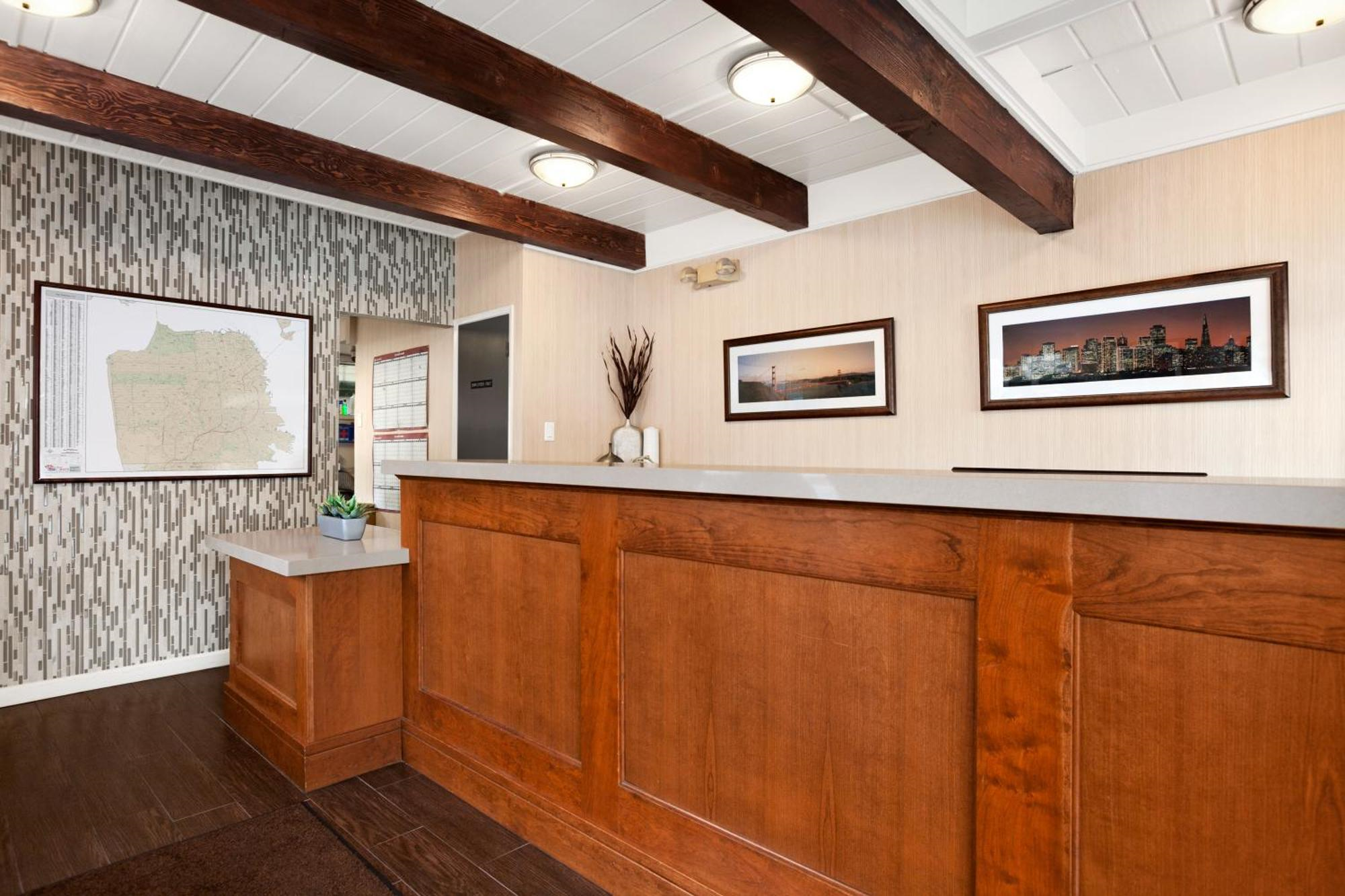 A wooden reception desk in a lobby with framed photos and a map on the wall, dark wood flooring, and overhead lights.