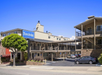 A Travelodge motel building with exterior corridors, parking spaces, and several parked cars under a clear blue sky.