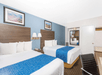 Hotel room with two double beds, blue and white bedding, a wooden headboard, wall art, a mirror, a chair, and a desk.