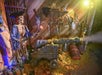 Pirate-themed display with a skeleton in pirate attire, a cannon on wheels, and various weapons on a wooden wall. Fake gold coins cover the floor. Dim, atmospheric lighting.