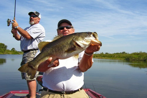Two men on the Trophy Bass fishing trip, holding a pole and their catch
