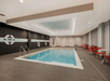 Indoor swimming pool with blue water, surrounded by gray tiles. Red chairs and tables line the right side. Walls are painted black and white with life rings as decoration.