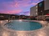 Outdoor hotel pool with lounge chairs, umbrellas, and a sunset sky.