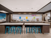 Self-serve frozen yogurt shop interior with long tables, blue stools, and colorful wall signage. Machines and topping options are lined up on the counter.