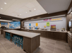 A modern breakfast bar with high tables and stools, featuring a variety of cereal dispensers, hot food items, and beverage stations under bright lighting.