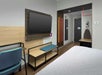 Hotel room with a wall-mounted TV, a desk and chair, an ironing board, and a bed with white linens.