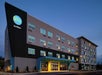 A four-story hotel building with "Tru by Hilton" signage, featuring modern architecture and large windows, under a clear evening sky.