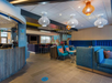 Modern hotel lobby with colorful seating, decorative light fixtures, and a check-in counter on the left.