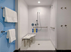 Accessible shower with a bench, grab bars, and handheld showerhead. Towels hang on wall hooks outside the shower. Various bottles are on a ledge.