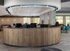 A wooden circular front desk in the middle of the lobby of the Tru by Hilton Orlando with a lounge area and windows in the background.