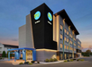 Modern hotel building with a "Tru by Hilton" sign, featuring a black facade, blue accents, and several floors of windows, set during dusk.