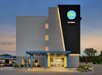 Front view of a Tru by Hilton hotel building with a modern facade, featuring a blue entrance canopy and illuminated signage. The surrounding area includes some greenery and a driveway.