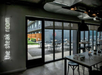 Indoor dining area with modern decor and a sign saying "the steak room." Large windows show an outdoor patio with tables and chairs.