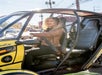 A woman with curly hair in a brown leather jacket sitting in the drivers seat of a GoCar on a sunny day in Las Vegas.