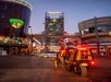 Two GoCars stopped at a stop light at night in Las Vegas with cars driving in front of them and a Las Vegas sign in the distance.