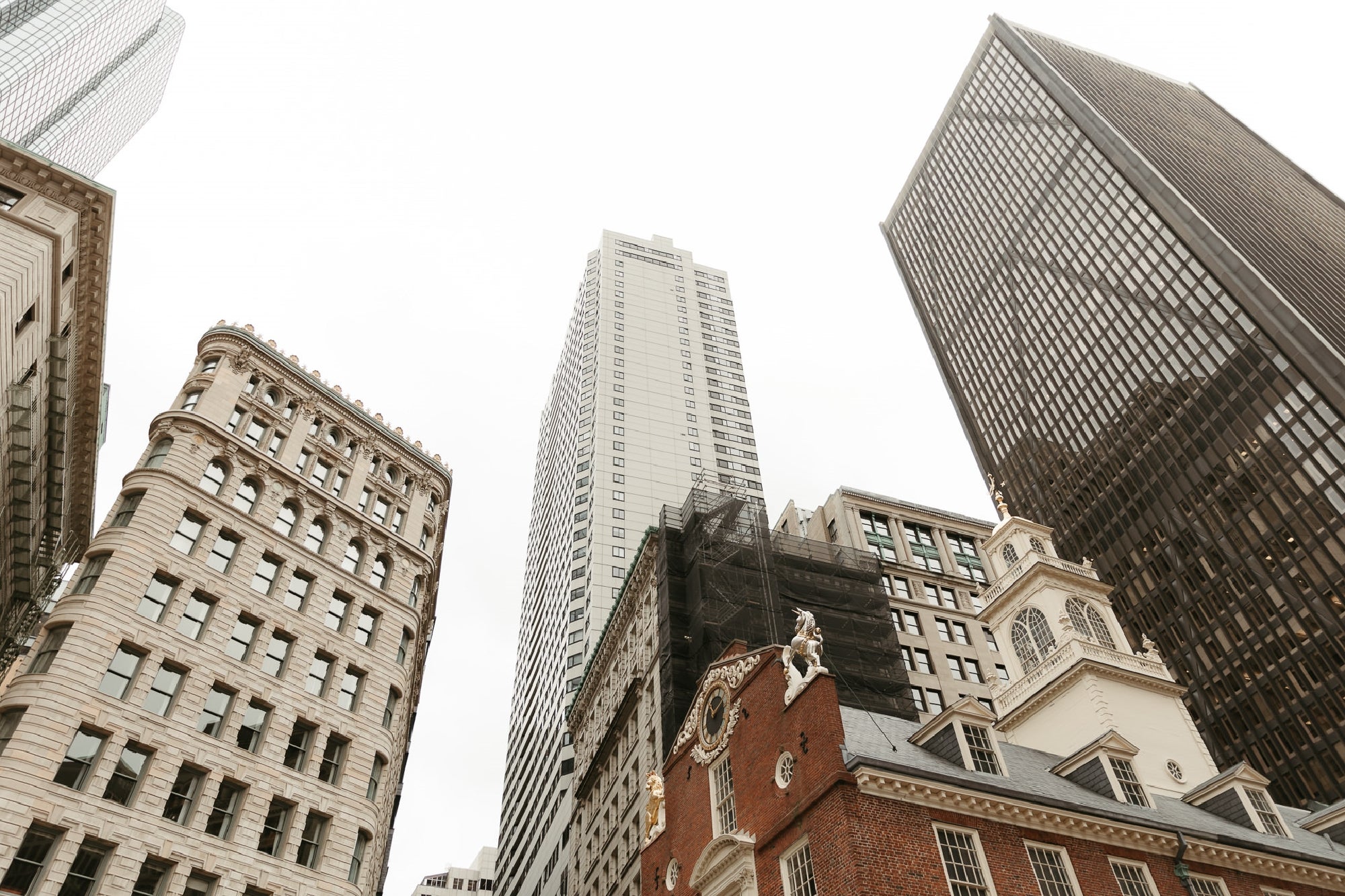 Several tall skyscrapers and historic buildings viewed from street level against a cloudy sky in a cityscape.