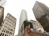 Several tall skyscrapers and historic buildings viewed from street level against a cloudy sky in a cityscape.