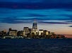 New York City skyline at dusk with illuminated skyscrapers reflecting on the water; One World Trade Center is the tallest building in the scene.