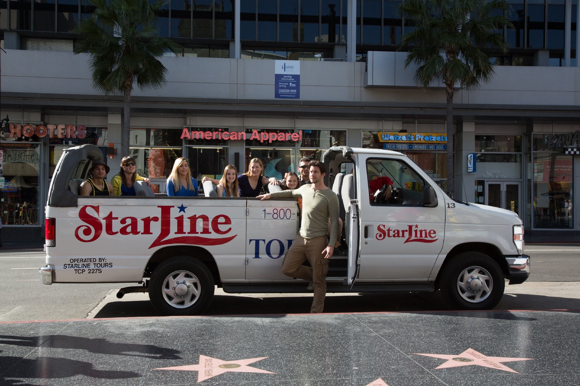 A group of people sits in an open-air StarLine tour van parked on a city street with palm trees and storefronts in the background.