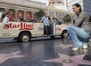 A woman crouches near stars on the Hollywood Walk of Fame while people sit in a StarLine tour van in the background.