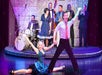 A man and woman dancing on stand with the man stand and the woman in the splits with a live band behind them at VEGAS! THE SHOW.