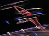 A woman in a small red and black dress with silver hula hoops spinning around her on stage at V - The Ultimate Variety Show.