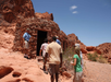A group of people approaches a small stone building in a rocky desert landscape under a clear blue sky.