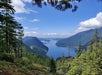 View of a forested mountain landscape with a river or inlet winding between hills under a blue sky with scattered clouds.