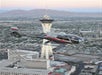 A black helicopter flies in front of the Stratosphere Tower above Las Vegas, with city buildings and mountains in the background.
