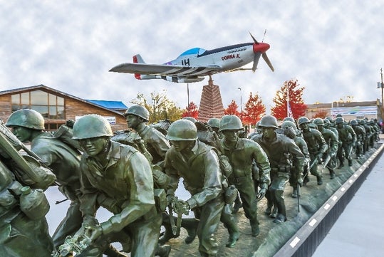 The P-51 "Donna K" soars above the "Storming the Beach" bronze statue.