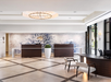 Modern hotel lobby with a chandelier, two reception desks, a large plant, and seating. A large mural depicting flowers adorns the back wall.