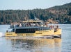 A yellow boat named "Prince of Whales" with passengers onboard, sailing near a forested shoreline.