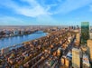 Aerial view of a city with a river running through it, flanked by tall buildings and urban landscape under a blue sky with scattered clouds.