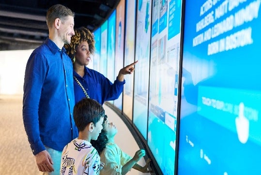 A family of four with two small children looking at an exhibit at the View Boston Observatory in Boston, Massachusetts.