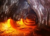 A lava tube with glowing orange light reflecting off the walls and floor, showing a curved, tunnel-like interior formed by volcanic activity.
