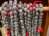 Close-up of leis made from black and white seed pods with red ribbons, hanging on a wooden rod.