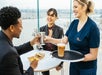 A couple seated at a table enjoys snacks while another woman serves them drinks at the Vue Orleans Cafe, situated on the 34th floor of the spectacular Vue Orleans 360° outdoor observation deck.