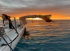 Person in a swimsuit and life jacket does a backflip off a boat into the ocean at sunset, while others watch and one person is in the water near the boat.