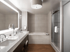Back-lighted mirror, bathtub, and glass-enclosed shower inside a private bathroom.