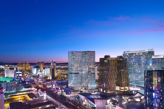 Aerial view of the Las Vegas Strip at dusk, featuring illuminated hotels and casinos with a clear sky transitioning from blue to purple.