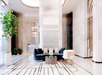 Luxurious lobby with marble floors, a central seating area featuring a blue sofa, white chairs, a round coffee table, and decorative plants. Modern lighting and tall columns enhance the space.
