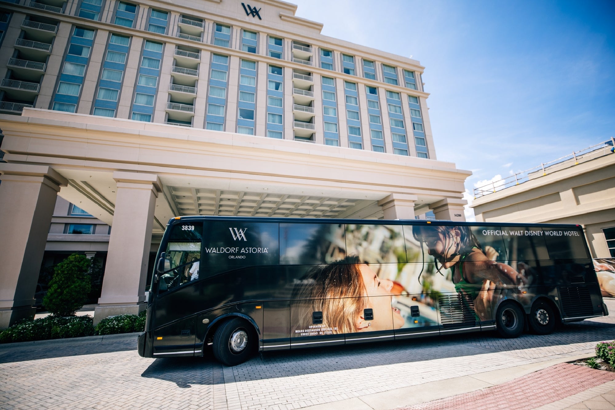 A Waldorf Astoria Orlando shuttle bus is parked in front of a hotel entrance, with the building's exterior and logo visible in the background.