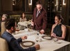 A waiter serves drinks to a man and woman seated at a table in an upscale restaurant, with other diners visible in the background.