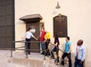 A tour guide opens a door for five people standing in line outside Stage 12 at a Warner Bros. studio lot.