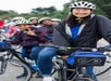 A group of people wearing helmets and jackets are smiling while sitting on bicycles. A logo reading "Unlimited Biking" is visible on a bike's pouch.