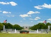 A sightseeing trolley is parked in front of the National World War II Memorial, with the Lincoln Memorial and two American flags in the background under a blue sky.