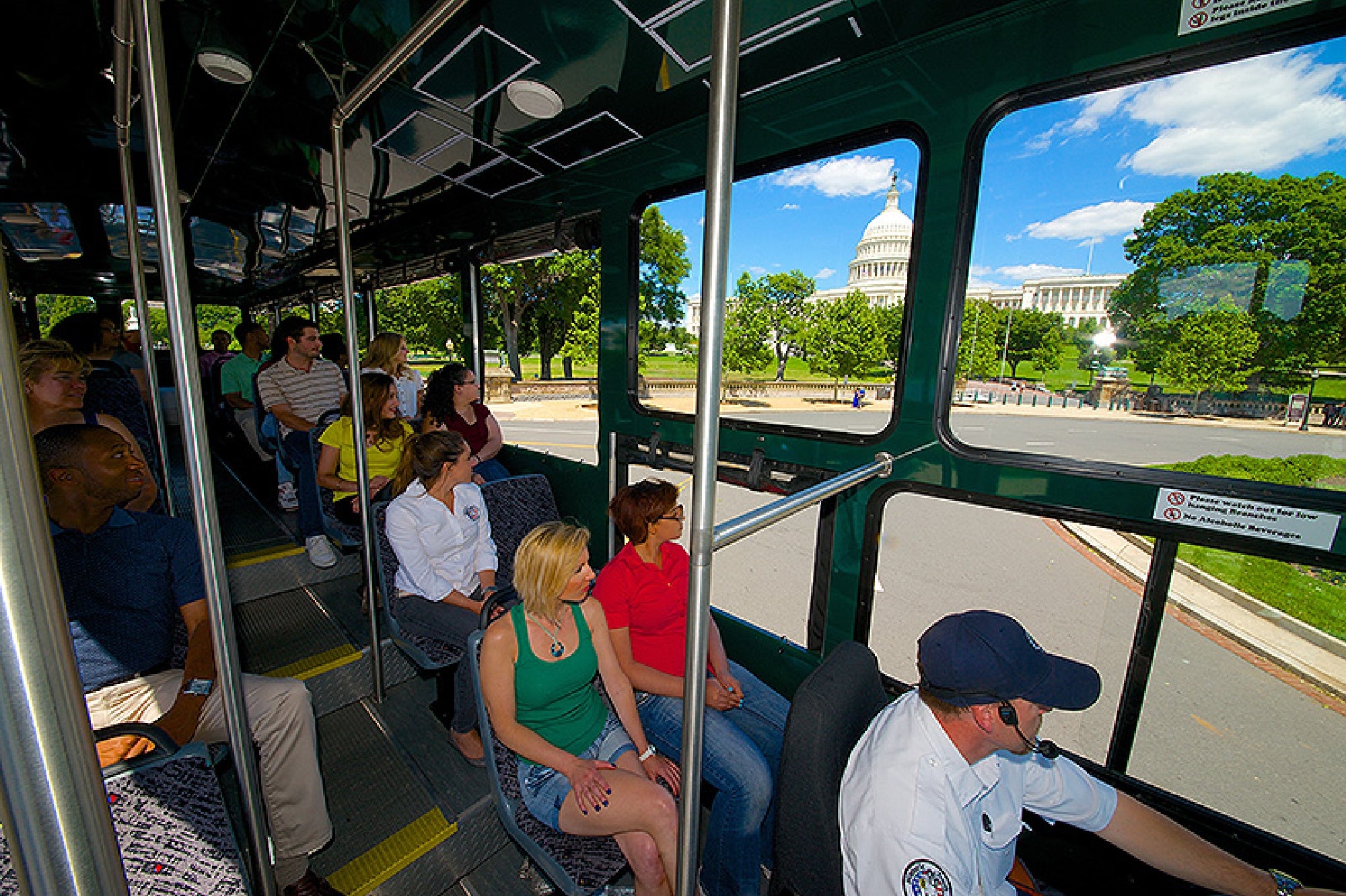 Passengers sit inside a tour bus as it drives past the United States Capitol building on a sunny day.